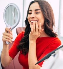 Woman smiling at reflection in handheld mirror