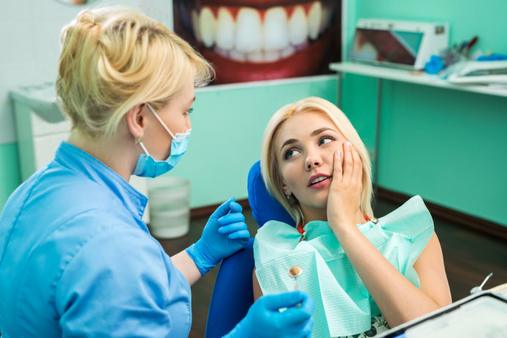 person holding cheek and speaking with emergency dentist