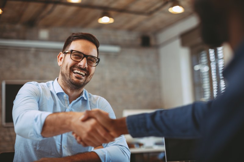 A man smiling and shaking hands with a client after his cosmetic dentistry treatments