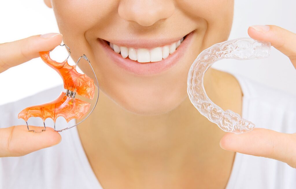 Nose-to-neck view of woman holding two types of retainers up to her face